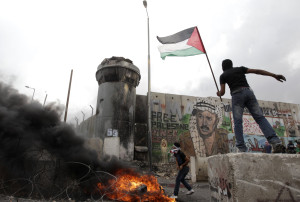 Palestinians hold a flag and throw a stone during clashes with Israeli troops at Qalandiya checkpoint