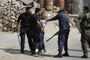 An Israeli soldier gestures as Palestinian policemen detain a youth during clashes in Hebron
