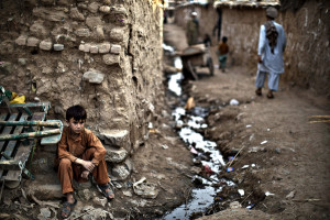 An Afghan refugee youth, sits on the side of the alley of a poor